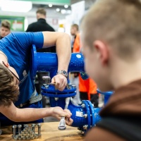 Ein Handwerker zeigt Kinder das befestigen von Rohren. Ein Handwerker zeigt Kinder das befestigen von Rohren.