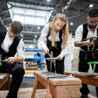 3 Handwerker:innen arbeiten an einer Schieferntafel. 3 Handwerker:innen arbeiten an einer Schieferntafel.