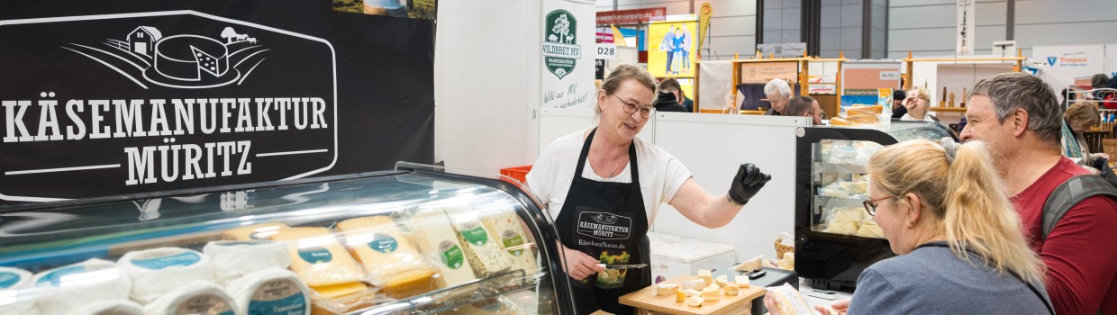 Eine Frau und ein Mann stehen an einem Verkaufsstand für Käse. Die Verkäuferin des Standes berät sie. Eine Frau und ein Mann stehen an einem Verkaufsstand für Käse. Die Verkäuferin des Standes berät sie.